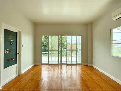Spacious room with wooden flooring and balcony view, perfect for versatile living space.