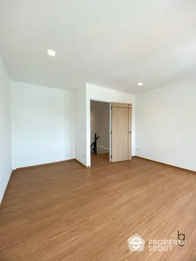 Spacious and well-lit empty room with hardwood flooring, white walls, and a large doorway leading to another room, perfect for versatile interior design.