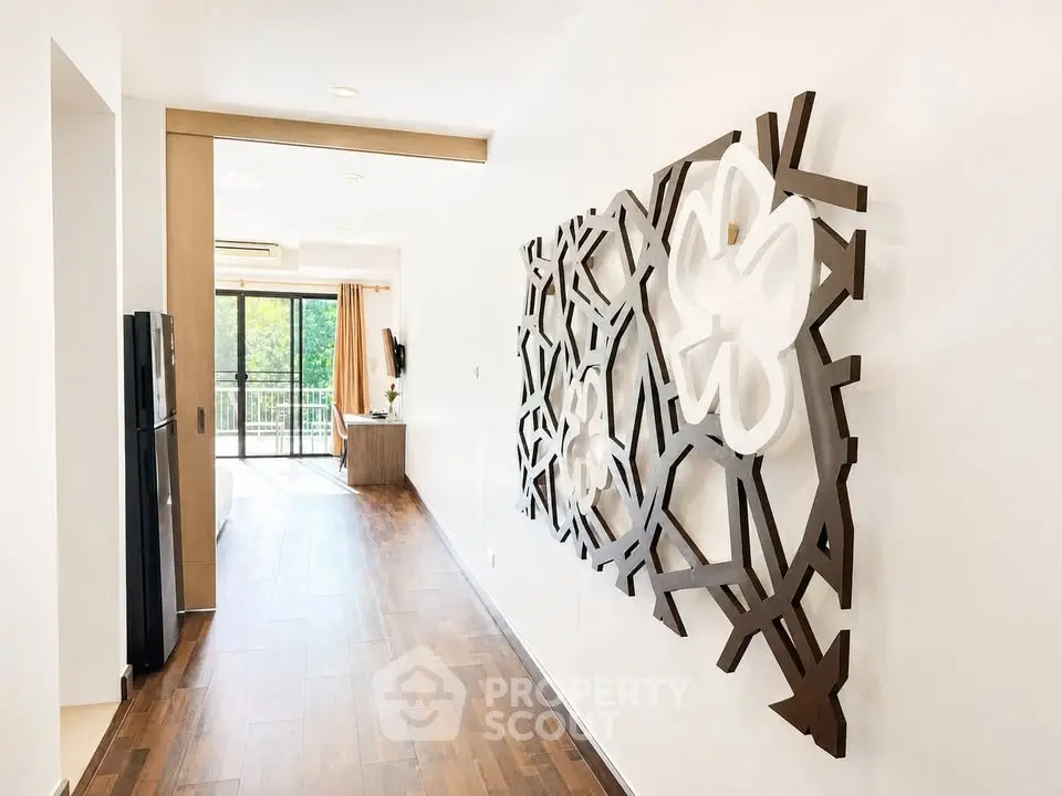 Spacious modern hallway with artistic wall decor and view of bright living area leading to balcony.