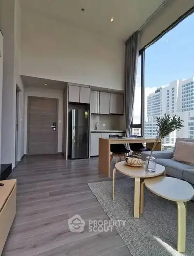 Modern open-plan living room with kitchen, large windows, and stylish decor in urban apartment.