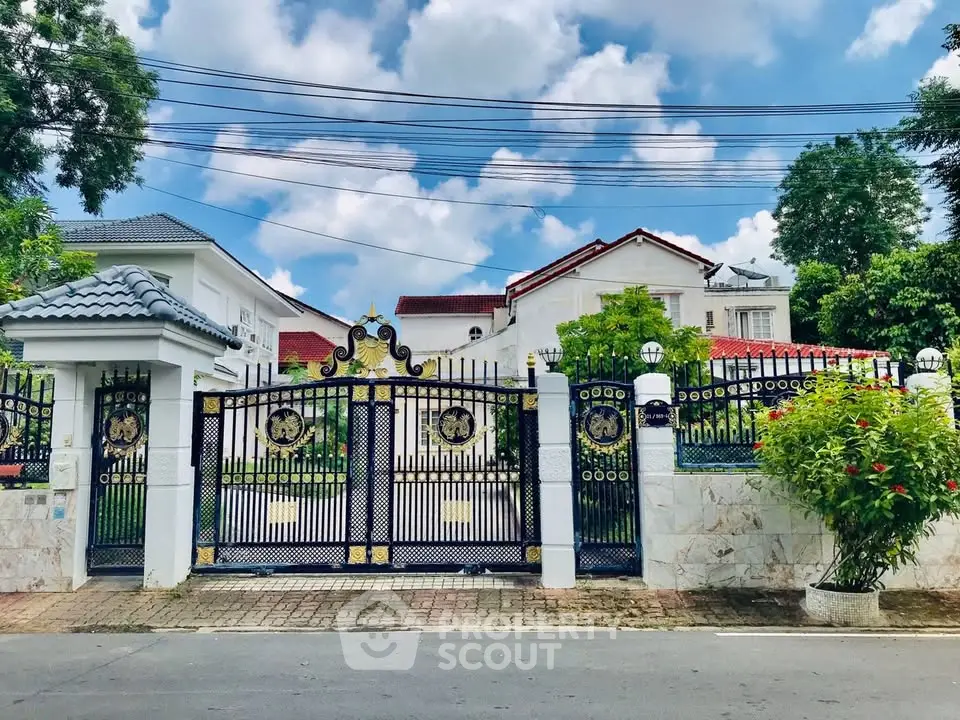Elegant gated entrance of a luxurious villa with lush greenery and blue sky.