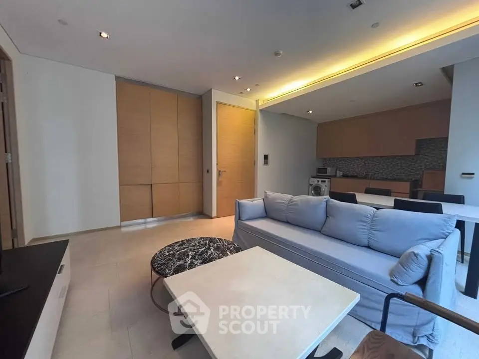 Modern living room with open kitchen, featuring sleek furniture and stylish lighting.