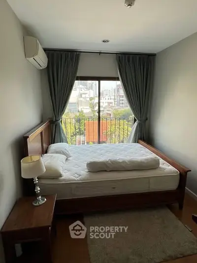 Cozy bedroom with city view, featuring a wooden bed frame, side table, and elegant curtains.