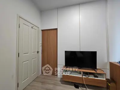 Modern minimalist living room with sleek white walls, wooden accents, and a flat-screen TV, ideal for cozy entertainment.