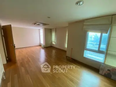 Spacious empty room with wooden flooring and large windows, perfect for customization.