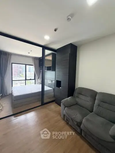 Modern apartment interior with cozy living room and bedroom separated by glass wall, featuring stylish furniture.