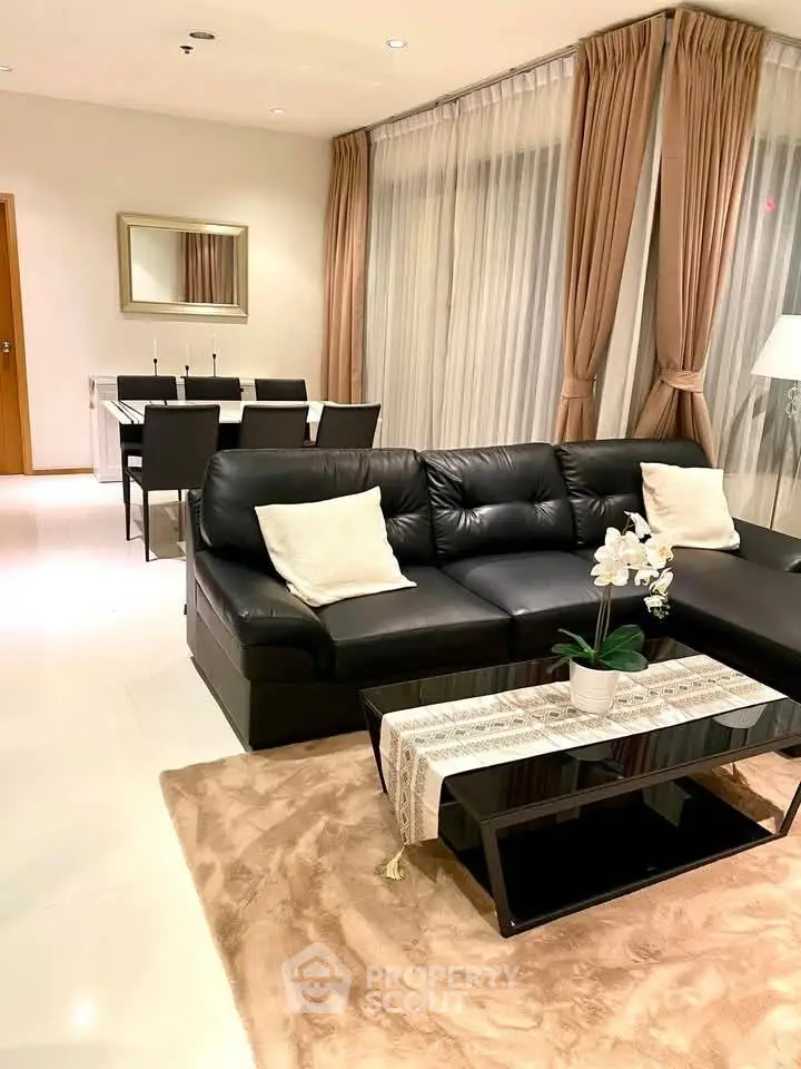 Elegant living room with black leather sofa and dining area, featuring modern decor and soft lighting.