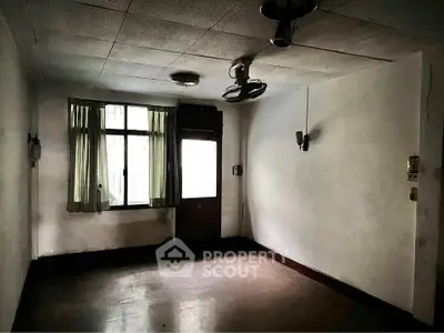 Spacious empty room with natural light and vintage ceiling fan, ideal for renovation.