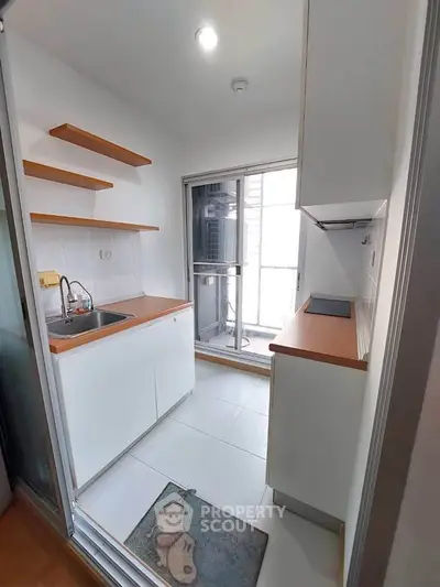 Compact kitchen with modern design and balcony access, featuring sleek countertops and open shelving.