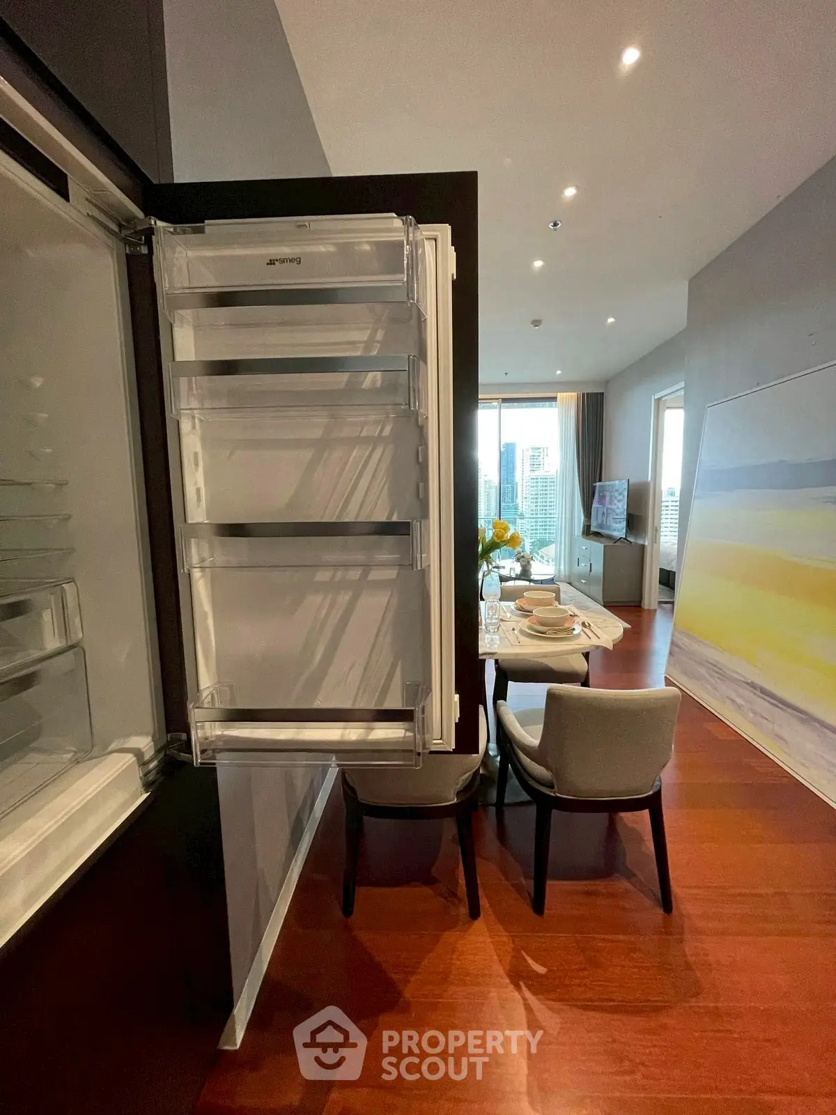 Modern open-plan living room with dining area and built-in fridge, featuring city views.