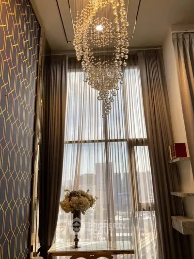 Luxurious high-ceiling interior with elegant chandelier and floor-to-ceiling windows offering city views.