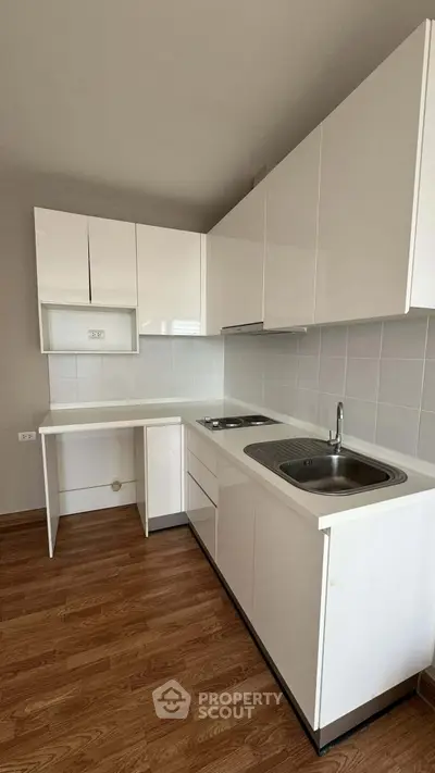 Modern kitchen with sleek white cabinets and wooden flooring, featuring a compact and efficient layout.