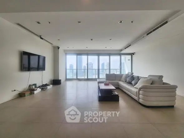 Spacious modern living room with large windows and city view, featuring a sleek sofa and wall-mounted TV.