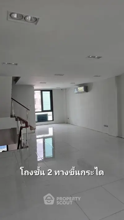 Spacious and well-lit empty living space with glossy tiled flooring, modern lighting fixtures, and a staircase leading to an upper level, perfect for customization.