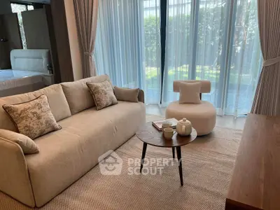 Elegant living room with cozy sofa, stylish chair, and garden view through large windows.