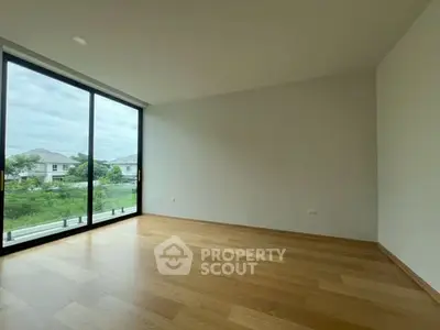 Spacious empty room with large windows and wooden flooring, offering a serene view.