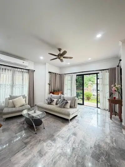 Spacious living room with elegant decor and garden view, featuring modern furniture and large windows.