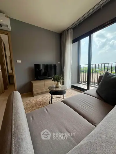Modern living room with large window and balcony view, featuring stylish furniture and natural light.