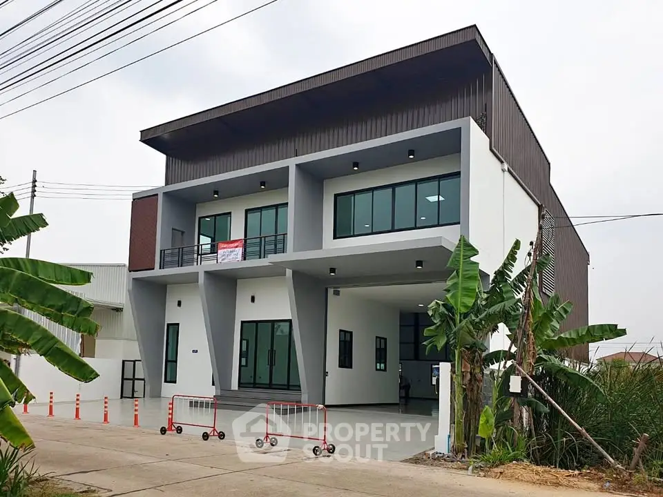 Modern industrial-style building with large windows and spacious parking area, ideal for commercial use.