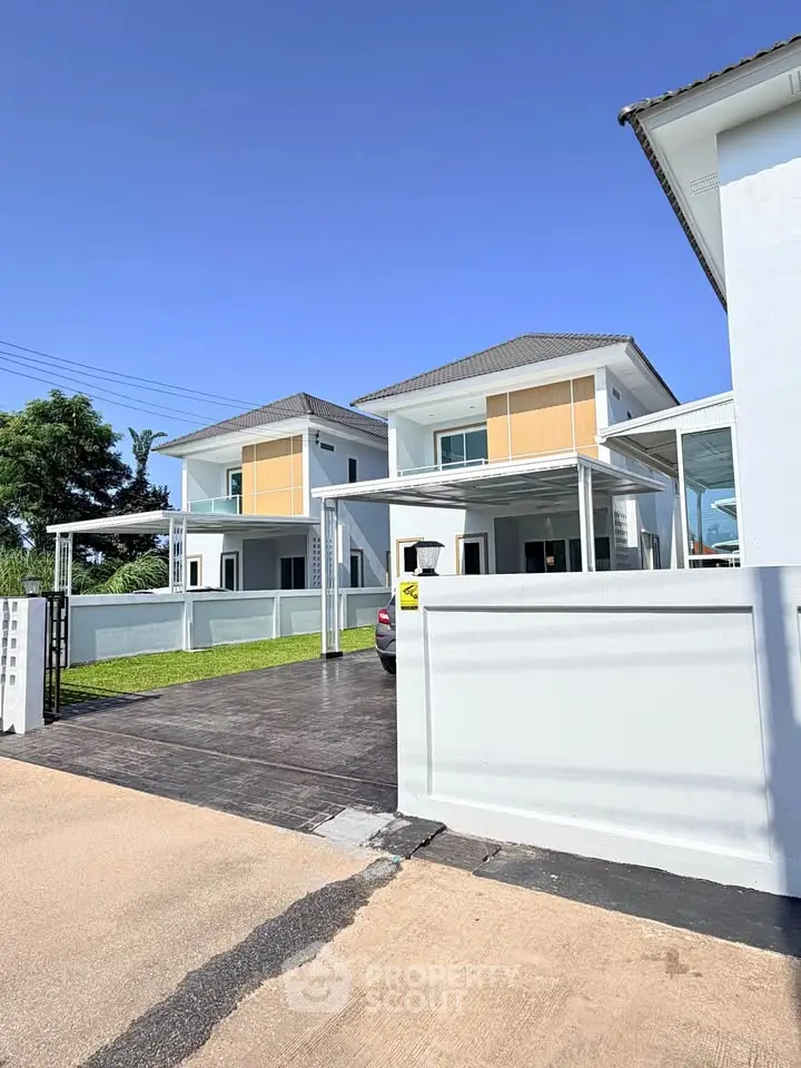 Modern two-story houses with carports and manicured lawns under a clear blue sky.