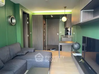 Modern living room with green walls, gray sectional sofa, and sleek kitchen area in open layout apartment.
