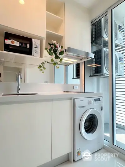 Modern kitchen with washing machine and microwave, sleek cabinetry, and bright lighting.