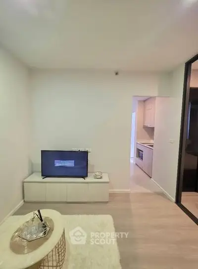 Modern living room with sleek TV setup and cozy decor, leading to a compact kitchen area.