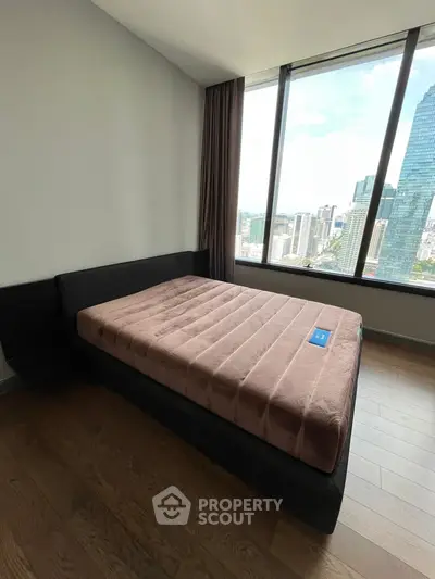 Modern bedroom with large window offering stunning city view, featuring a sleek bed and hardwood floors.