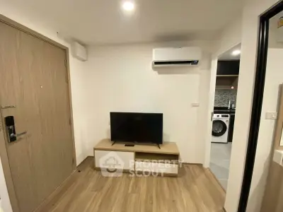 Modern living room with TV, air conditioning, and view into kitchen with washing machine.