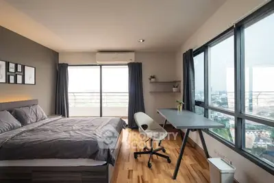 Modern bedroom with large windows and city view, featuring a stylish desk and comfortable bed.