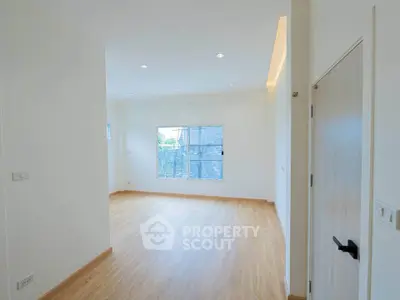 Spacious empty room with wooden flooring and large window, perfect for customization.