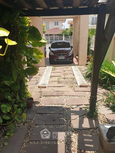 Charming garden pathway leading to a secure parking area with lush greenery and modern vehicle.