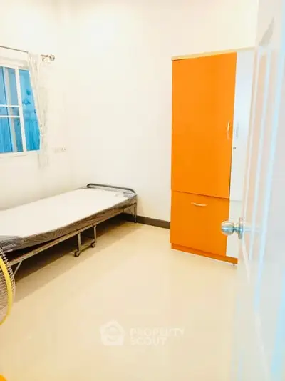 Bright minimalist bedroom with single bed and vibrant orange wardrobe