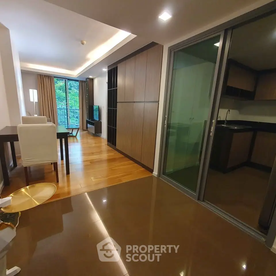 Modern living room with open layout and sleek kitchen design, featuring wooden flooring and large windows.