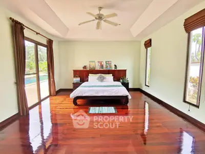 Spacious bedroom with polished wooden floors and pool view, perfect for luxury living.