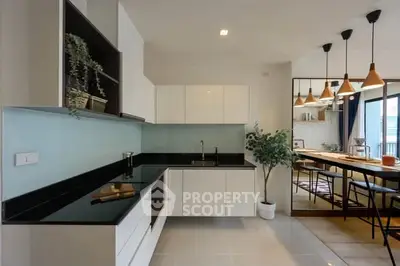 Modern kitchen with sleek black countertops and open layout, featuring stylish pendant lighting and dining area.