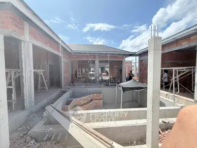 Under-construction modern house with brick walls and open layout under a clear blue sky.