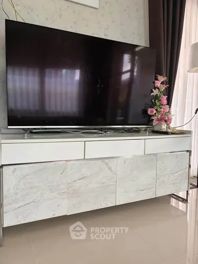 Modern living room with sleek TV stand and large flat-screen TV, elegant decor and polished flooring.