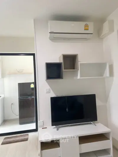 Modern living room with air conditioning and sleek TV setup, adjacent to a compact kitchen area.