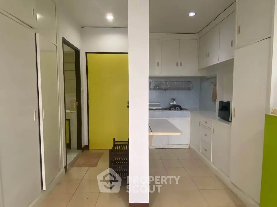 Compact kitchen with white cabinets and yellow door, featuring a small dining area.