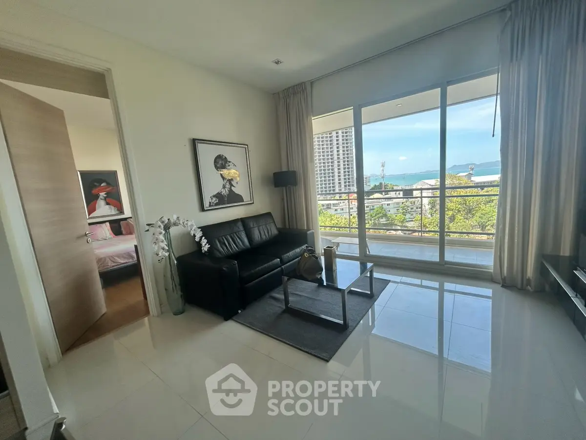 Modern living room with sleek black sofa, large window offering stunning ocean view, and elegant decor.