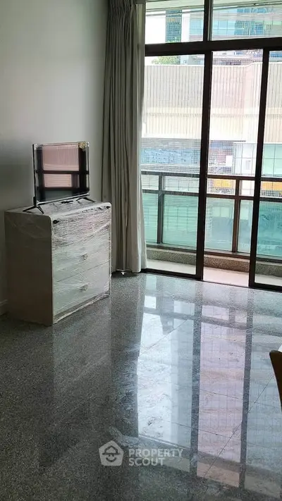 Spacious living room with large windows and natural light, featuring a TV and modern decor.