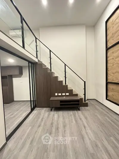 Modern duplex interior with sleek staircase and glass railing, showcasing open space and contemporary design.