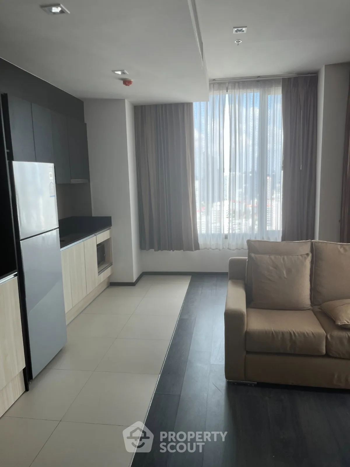 Modern apartment interior with sleek kitchen and cozy living area, featuring large windows and natural light.