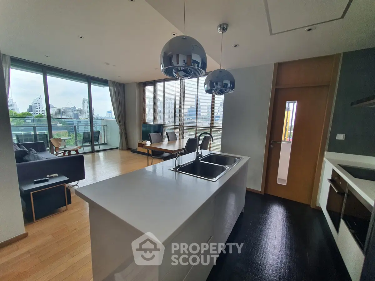 Modern open-plan living room with sleek kitchen and city view balcony.