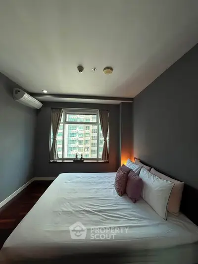 Spacious bedroom with large window offering city view, featuring modern decor and cozy ambiance.