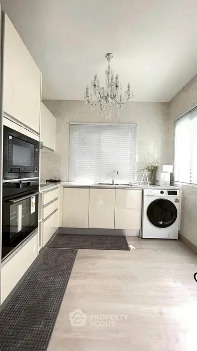 Modern kitchen with chandelier, oven, and washing machine in sleek design.