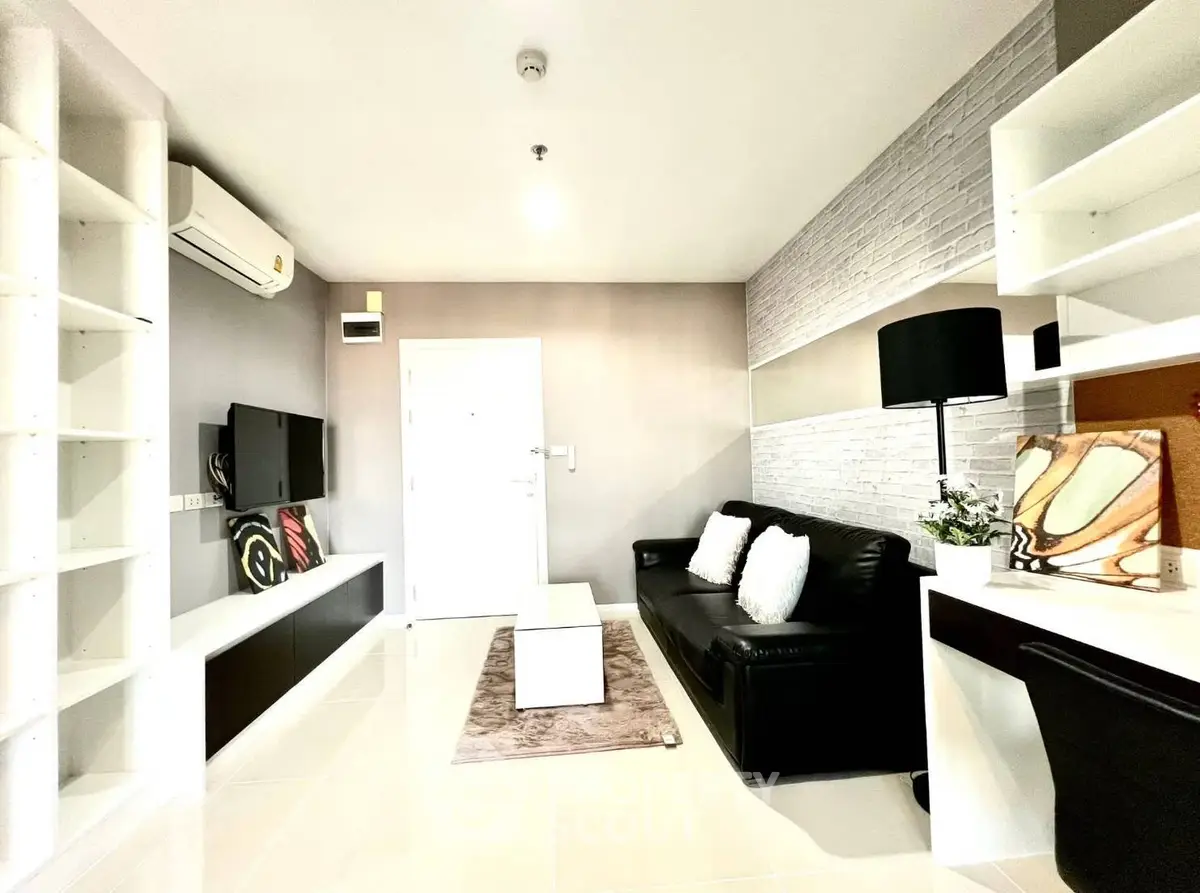 Modern living room with sleek black sofa and wall-mounted TV, featuring stylish decor and ample shelving.