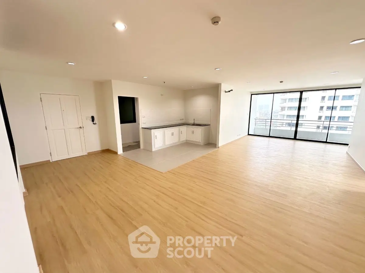 Spacious open-plan living area with wooden flooring and large windows offering city views.