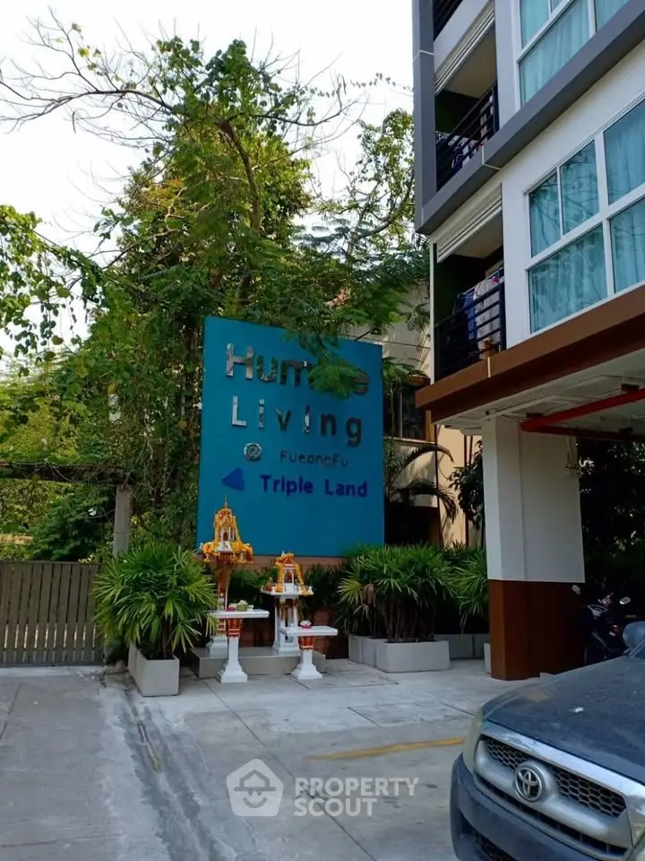 Modern apartment building entrance with lush greenery and stylish signage.